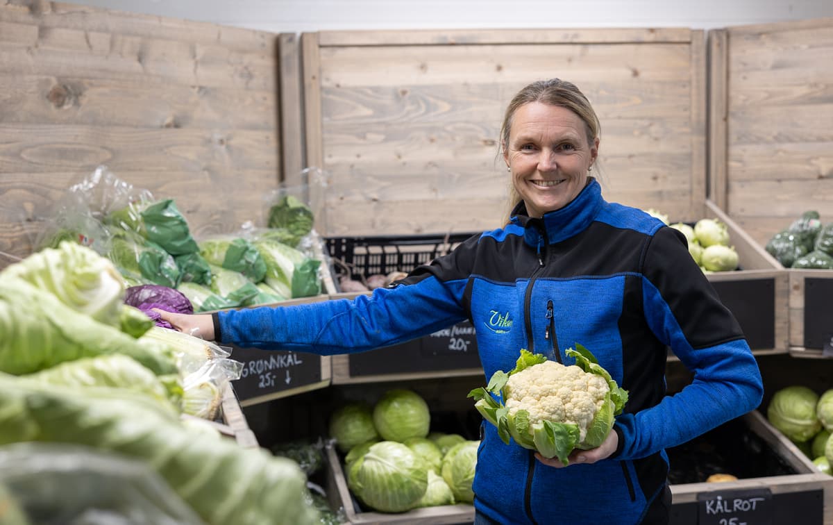 Smilende dame omringet av grønnsaker, holdende på et blomkålhode Smilende dame omringet av grønnsaker, holdende på et blomkålhode