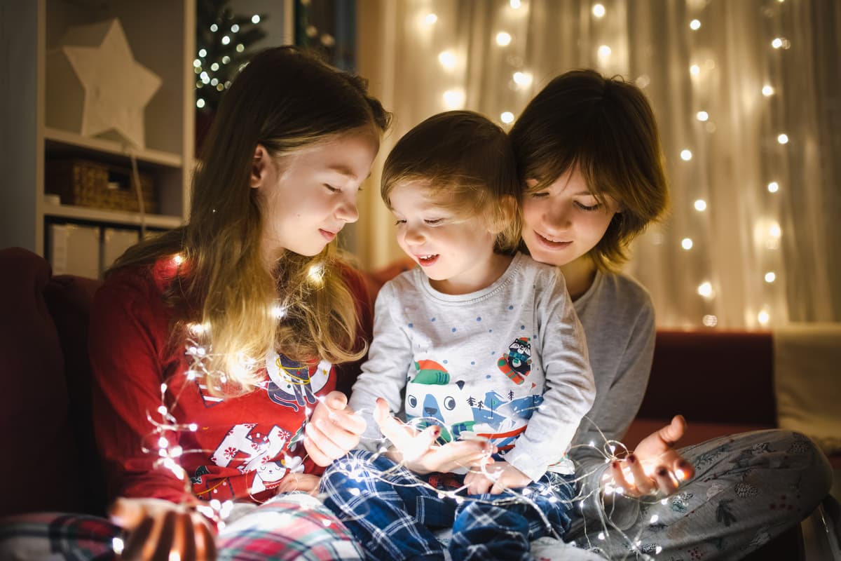 Tre barn i pysj i stue med julelys Tre barn i pysj i stue med julelys