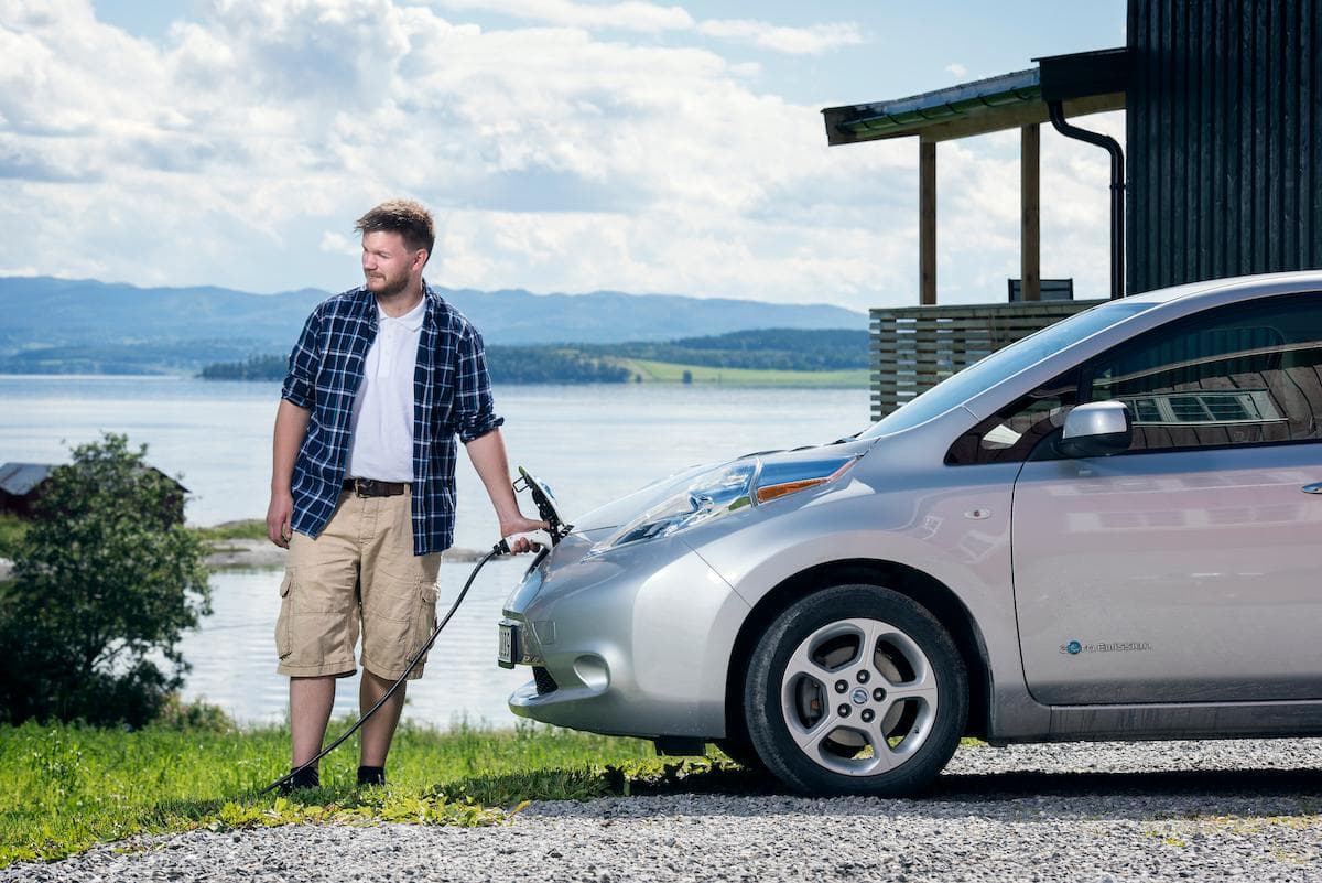Elbillading En mann holder fast i en lader som er plugget i en elbil