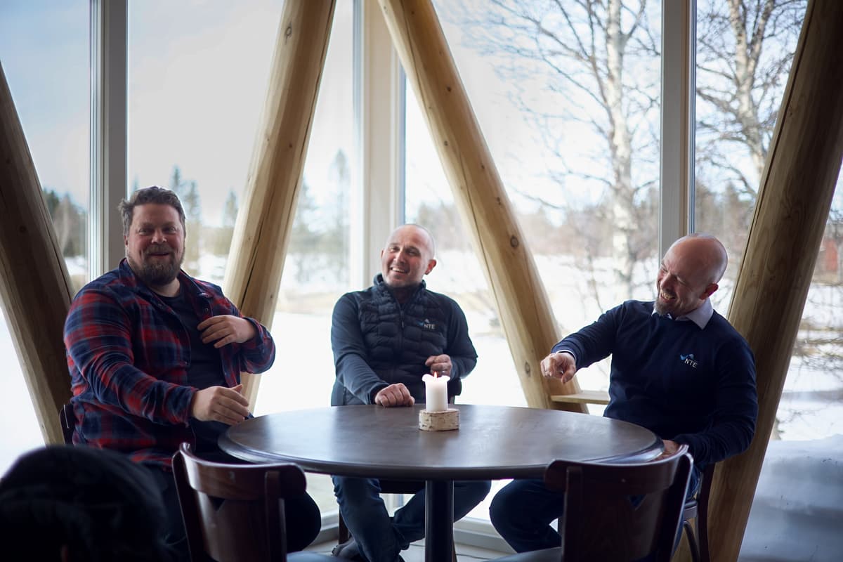 God stemning rundt bordet Tre menn sitter rundt et bord og ler