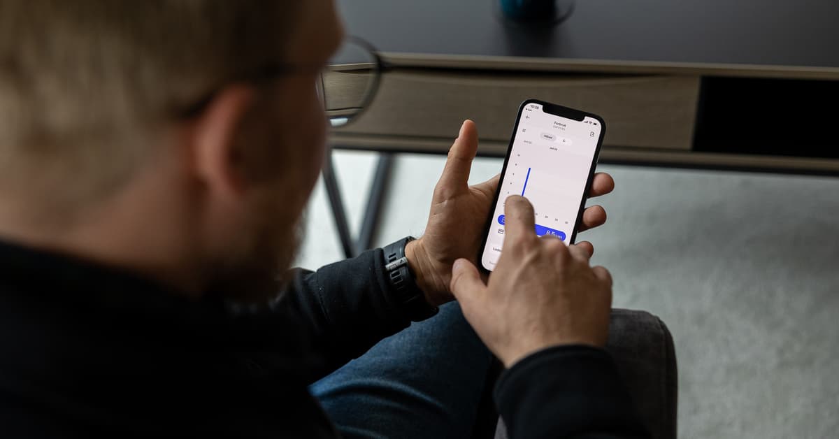 Mann holder en mobil som viser forbruksdata på elbillading Mann holder en mobil som viser forbruksdata på elbillading