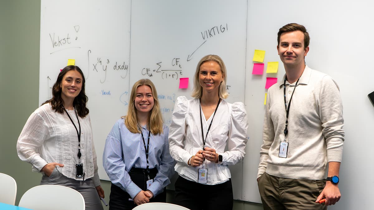 Tre kvinner og en mann foran en tale med regnestykker Tre kvinner og en mann foran en tale med regnestykker