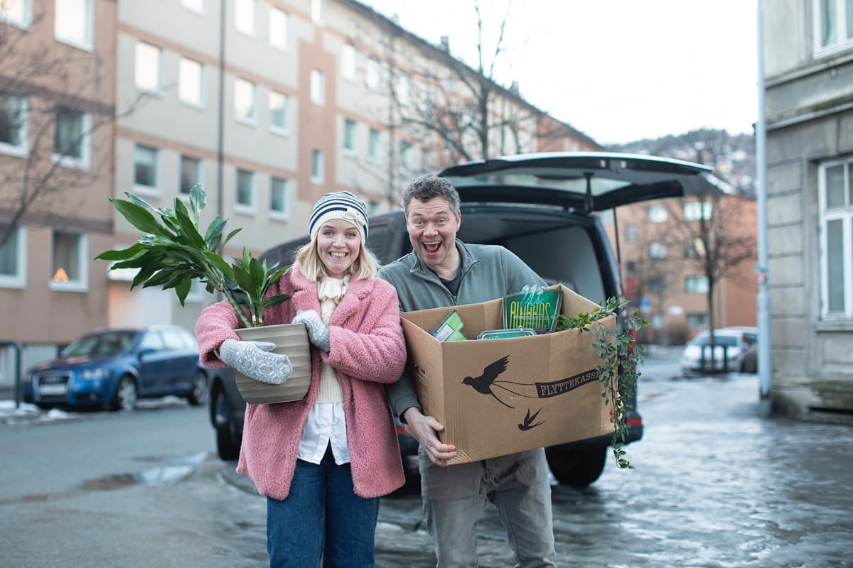 Et par står med flytteesker foran en boligblokk Et par står med flytteesker foran en boligblokk