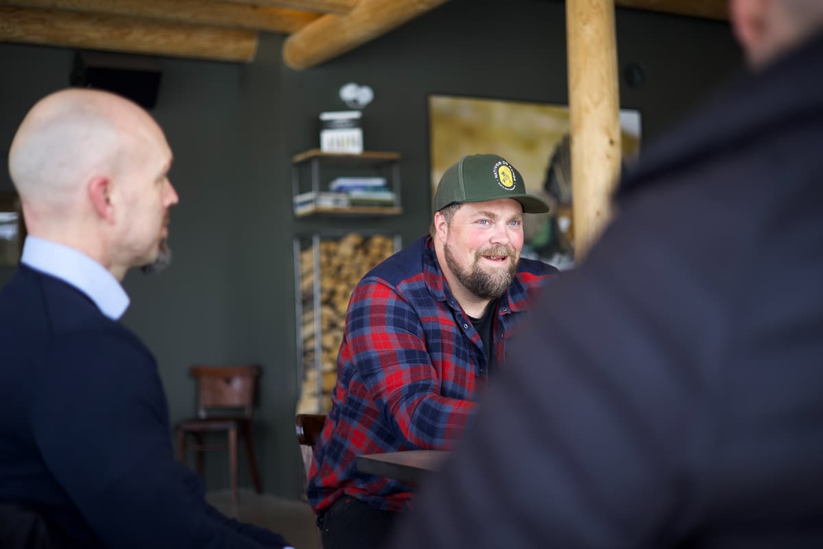 Ole Fredrik Haarsaker Smilende mann med caps i samtale med to menn du ser bakhodet på