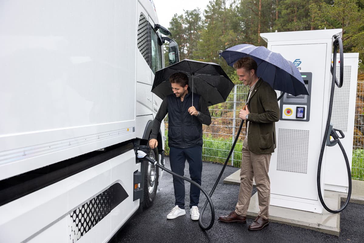 To menn med paraply plugger i laderen på en elektrisk lastebil To menn med paraply plugger i laderen på en elektrisk lastebil