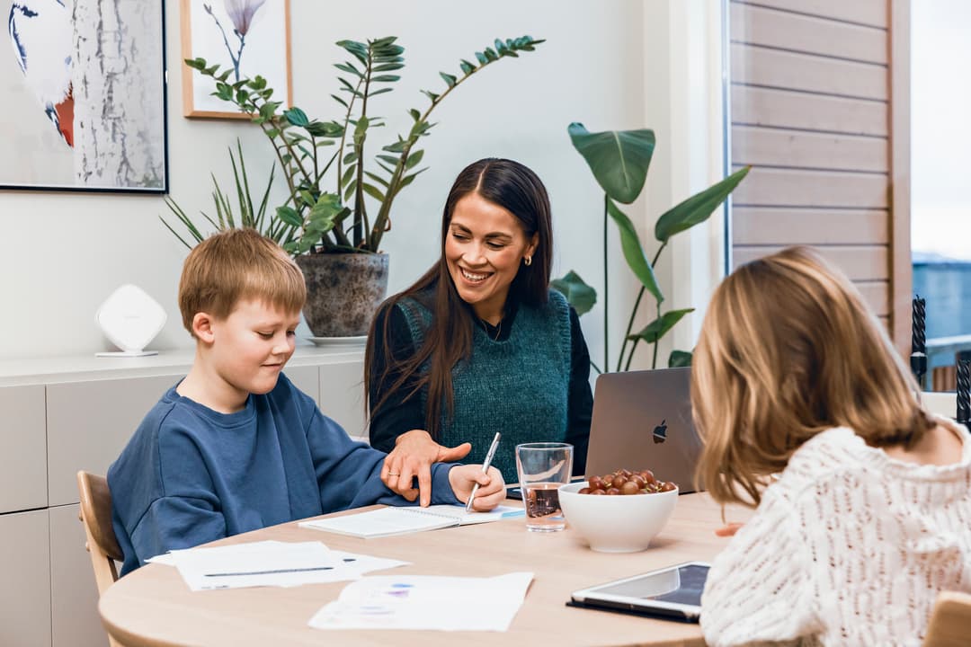Mor og barn gjør lekser Bilde av mor og to barn som sitter ved et bord. Mor hjelper sønnen med lekser. Datteren ser på et nettbrett.