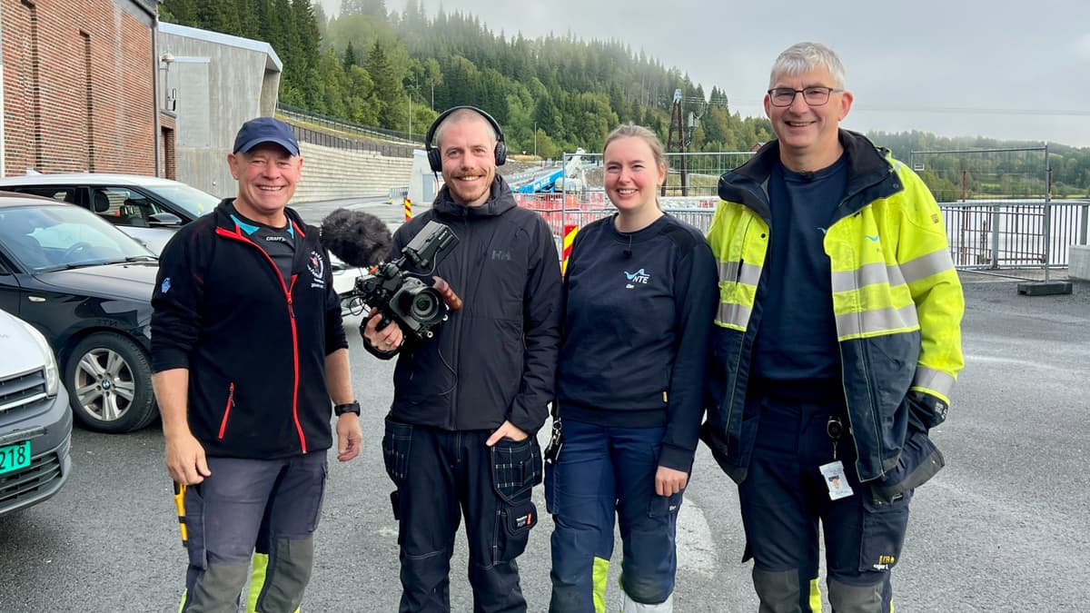 Fire personer står oppstilt og smiler. Den ene har et filmkamera. Foto. Fire personer står oppstilt og smiler. Den ene har et filmkamera. Foto.