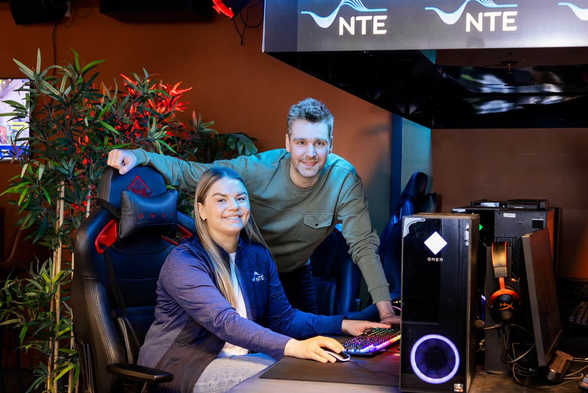 Alex Hole og Marte Melhus To smilende menn står på hver sin side av en blid dame. I bakgrunnen ser du ungdommer som sitter og gamer.