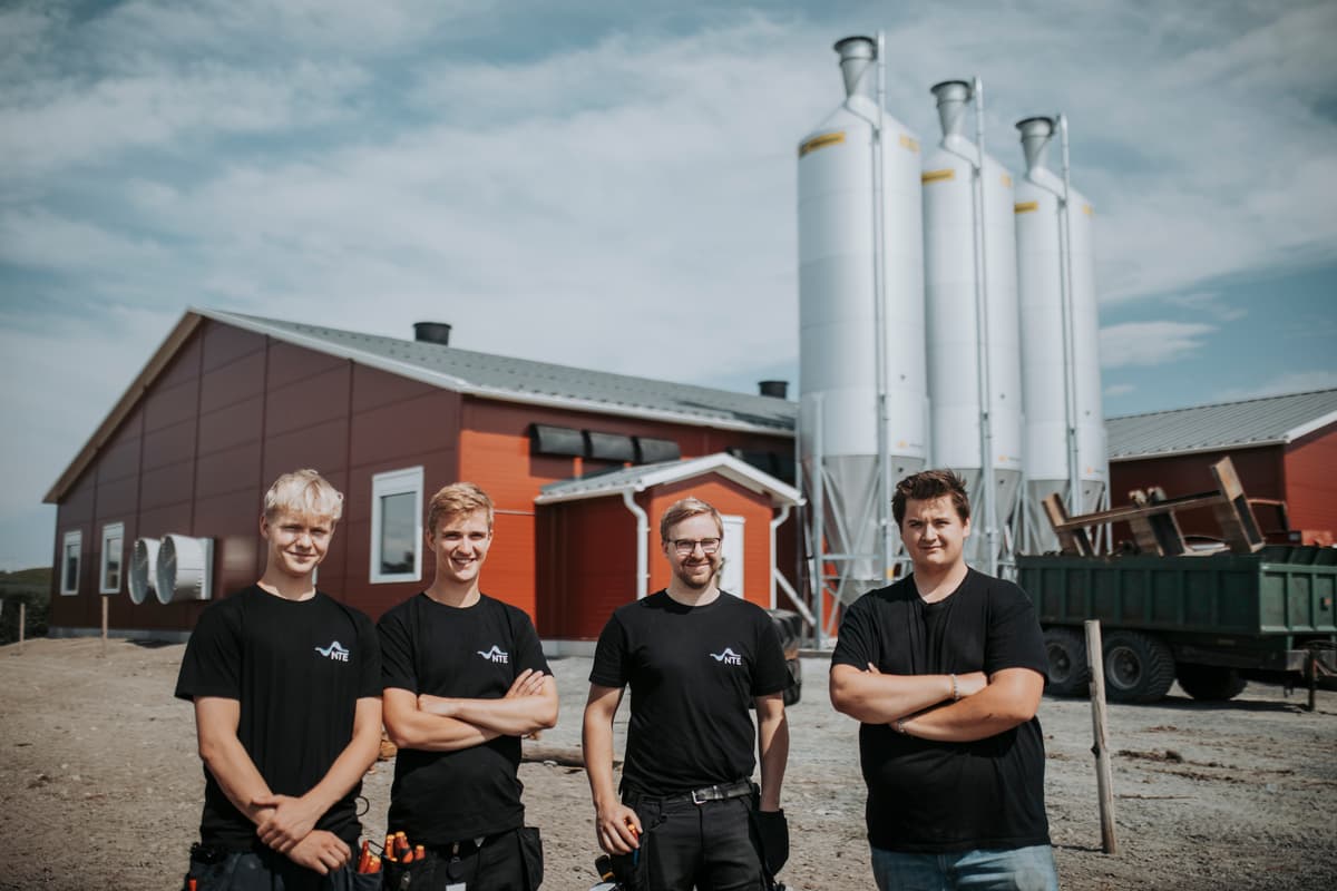 Fire smilende menn foran et fjøs og 3 siloer Fire smilende menn foran et fjøs og 3 siloer